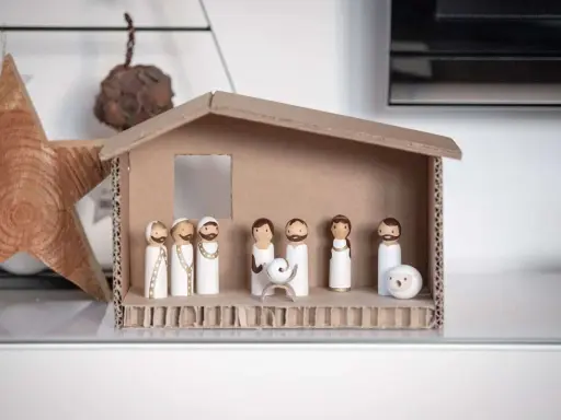 Eine einfache Krippe basteln Kinder mit Holzfiguren und Karton. Maria, Josef und das Jesuskind sind in der Mitte, umgeben von Hirten und einem Schaf.