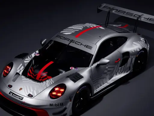Silberner Porsche 911 GT3 R mit auffälligem Schachbrettmuster und roten Akzenten, bereit für die Rennstrecke.