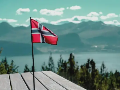 Norweska flaga na tle gór i jeziora. Pomyśl o tym, jak wysłać zwolnienie lekarskie do NAV, gdy jesteś w tak pięknych okolicznościach.