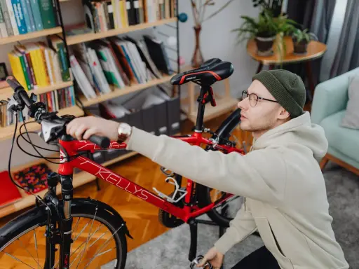 Mężczyzna przygotowuje rower do wysyłki w całości. W tle regał z książkami i rośliny.