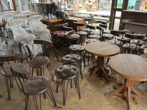 Viele gebrauchte Gastrostühle und runde Holztische stehen in einem Raum.