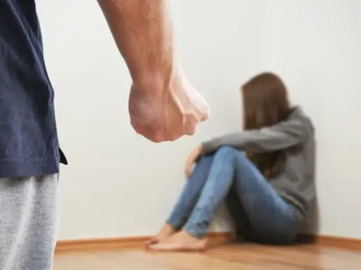 Zaciśnięta pięść mężczyzny grozi skulonej kobiecie. Scena symbolizuje agresję żony wobec męża, przemoc domową.