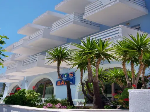 Hotel na Krecie z białymi balkonami i palmami.