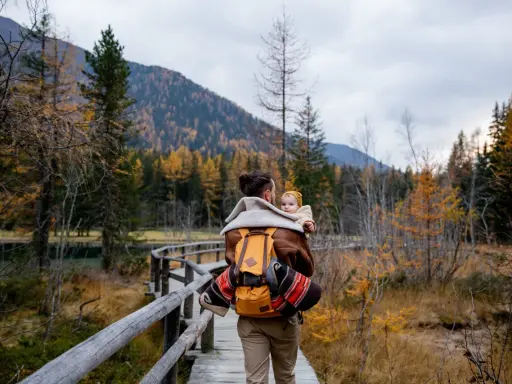 Ojciec z dzieckiem na plecach spaceruje drewnianą kładką pośród jesiennych lasów. Tatry z dzieckiem to piękna przygoda.