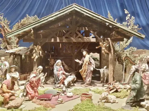 Krippenszene mit Maria, Josef und dem Jesuskind. Engel schweben über der Szene, die an Weihnachten im Mittelalter erinnert. Hirten und Musiker sind versammelt.