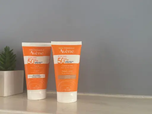 Deux tubes de spray solaire invisible SPF 50 Avène, l'un teinté, l'autre non, pour une protection optimale.