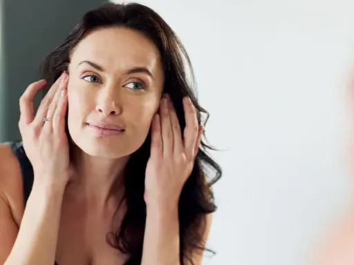 Mujer se toca la cara, examinando su piel. No se observa ninguna cara inflamada.