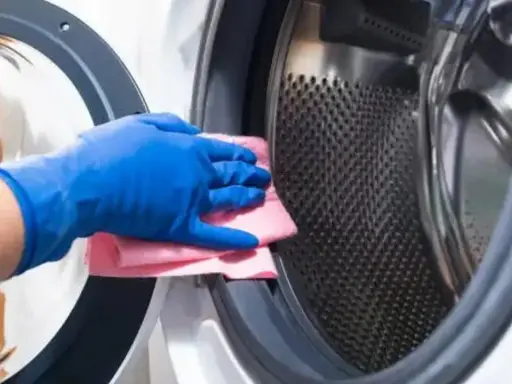 Mano con guante azul limpiando la goma de la lavadora con un paño rosa.