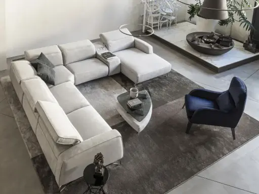 Ampio soggiorno con un grande divano modulare di colore chiaro, un tappeto scuro e un pavimento chiaro. Un poltrona blu e un tavolino completano l'arredo.