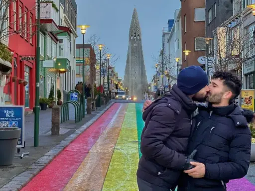 A couple shares a kiss on a rainbow-painted street in gay Reykjavik, with Hallgrímskirkja church in the background.