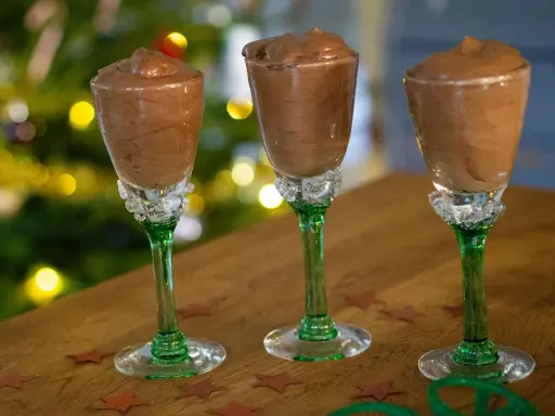Tre glas med krämig chokladmousse, perfekta för ett enkelt chokladmousse recept. Julbelysning i bakgrunden skapar en festlig stämning.