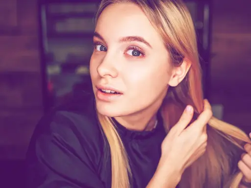 Junge Frau mit blonden Haaren, die sich die Haare für die Olaplex No. 0 Anwendung zurechtmacht.