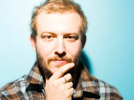 Bon Iver Sverige: en man med skägg och flanellskjorta funderar mot en turkos bakgrund.