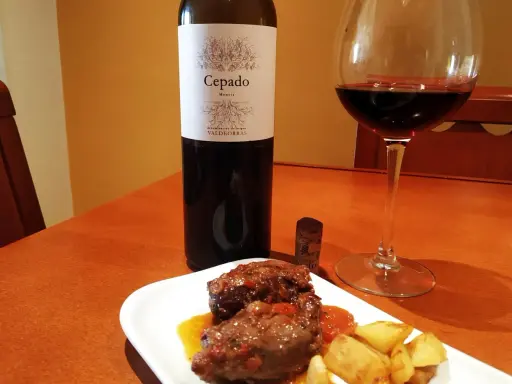 Un plato de carrilleras estofadas con patatas, acompañado de una copa de vino tinto Cepado Mencía, ideal para maridar.