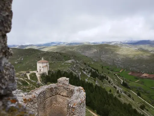Un piccolo santuario domina il paesaggio del **cammino del Gran Sasso**, tra colline verdi e montagne nebbiose.