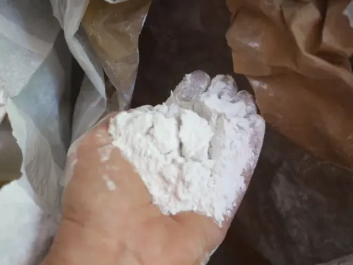 Main d'une personne tenant une poudre blanche fine, de la chaux morte, sortant d'un sac en papier.