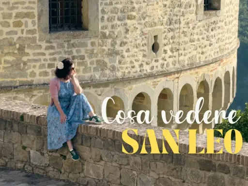 Donna seduta su un muretto di pietra, con vista panoramica. Un'ottima pausa durante il trekking a San Leo.