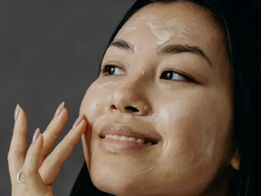 Donna applica una crema sul viso, un gesto quotidiano per come curare la pelle del viso.