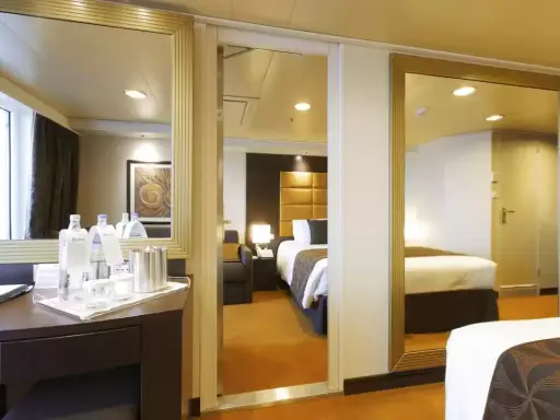Interno di una cabina MSC Divina con balcone. Letto, specchi e un tavolino con bottiglie d'acqua.