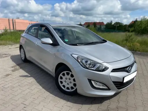 Srebrny Hyundai i30 1.4 benzyna zaparkowany na kostce brukowej, w tle zielona trawa i budynki.