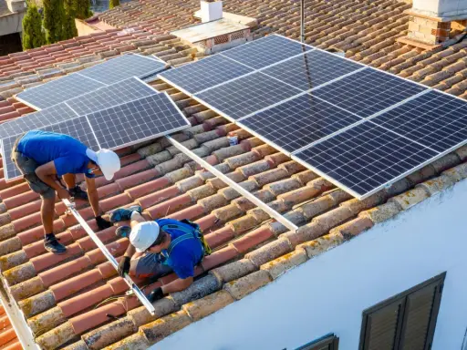 Dos técnicos instalan placas solares en un tejado. Aprendiendo como instalar placas solares para un futuro energético.