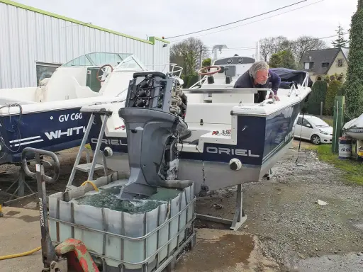 Un homme effectue le rinçage moteur hors bord vinaigre blanc d'un bateau. L'hélice est immergée dans une cuve remplie de liquide.