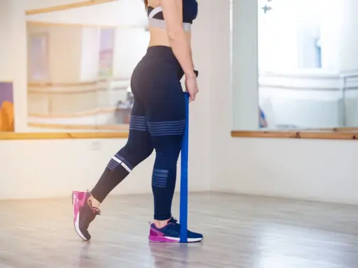 Frau trainiert Beine mit Widerstandsband. Sanftes, gelenkschonendes **low impact training** für Kraft und Ausdauer.