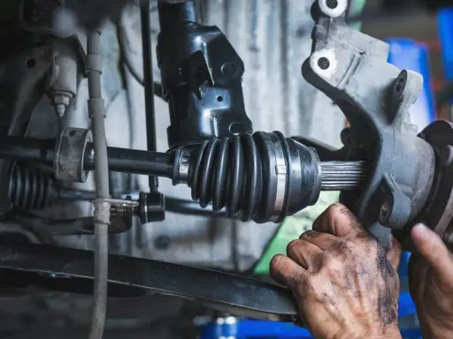 Mechanik wymienia uszkodzoną półoś, która powoduje wibracje. Widać gumową osłonę przegubu i zębaty wałek.
