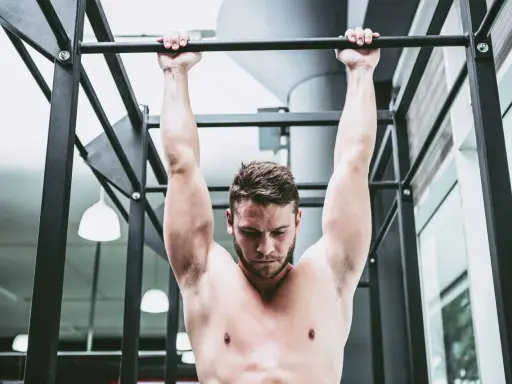Uomo a torso nudo esegue trazioni alla sbarra, concentrato sul movimento per rafforzare la muscolatura.