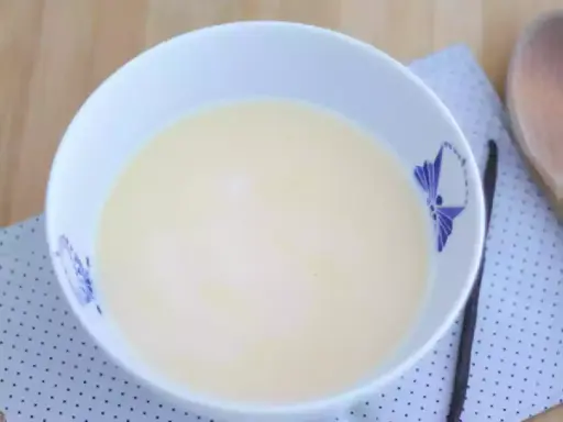 En skål med krämig vaniljsås, perfekt för ditt vaniljsås recept. En vaniljstång ligger bredvid.