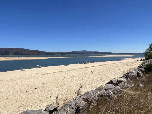 Gente disfrutando del sol y el agua en la playa de Arija, con montañas al fondo y un cielo azul despejado.