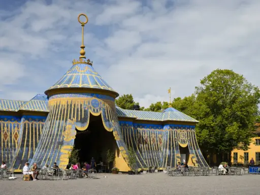 Blå och guldfärgad cirkustältliknande byggnad med uteservering i Haga parken.