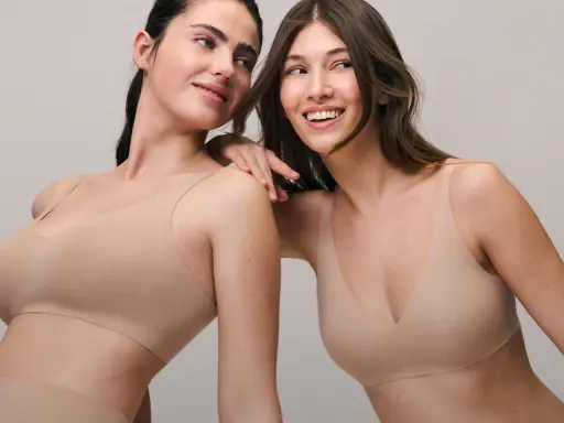 Due donne sorridono, indossando top color carne che valorizzano il décolleté. Un'immagine che ispira su come avere un bel seno con comfort e stile.