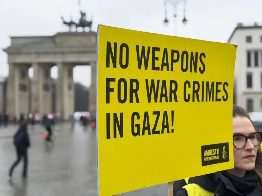 Gelbe Tafel mit Aufschrift "NO WEAPONS FOR WAR CRIMES IN GAZA!" vor dem Brandenburger Tor. Amnesty International setzt sich für Menschenrechte ein.