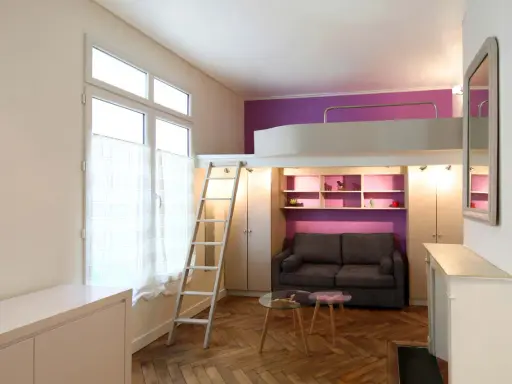 Aménagement petit studio optimisé avec lit mezzanine, canapé confortable et rangements intégrés. Un espace de vie fonctionnel et stylé.