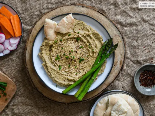 Hummus de berenjena cremoso, decorado con sésamo y espárragos, acompañado de pan de pita y crudités.