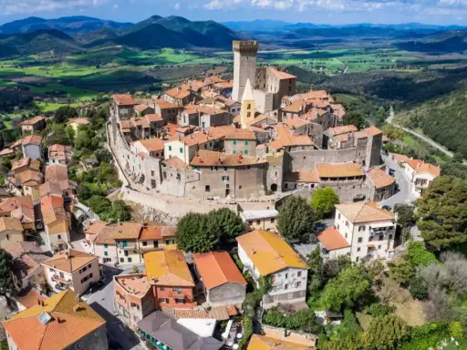 Un borgo medievale con un castello domina le colline toscane. Perfetto per un weekend in Toscana, tra tetti rossi e panorami mozzafiato.