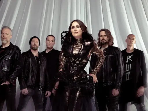 Within Temptation Sverige: Sharon den Adel i sin glittrande klänning, omgiven av bandmedlemmar i mörka kläder, framför en vit draperad bakgrund.