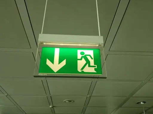 Zielony znak oświetlenia awaryjnego i ewakuacyjnego z ikoną strzałki w dół i biegnącej postaci.