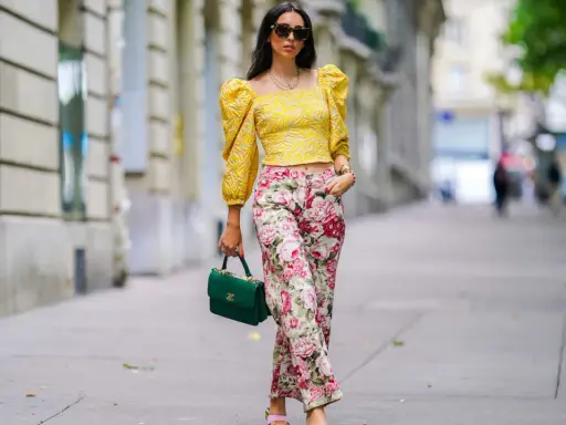A woman shows that a woman can wear pants for cocktail attire, sporting a yellow puff-sleeve top and floral pants.