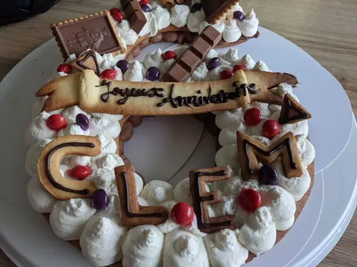 Gâteau d'anniversaire en forme de chiffres, décoré de crème fouettée, de biscuits lettres formant "CLEM", de chocolats et de bonbons. Quelle crème pour recouvrir un gâteau ? Celle-ci est parfaite !