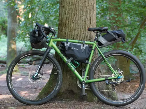Grünes Gravelbike mit Taschen für Bike Packing, bereit für Abenteuer im Wald.