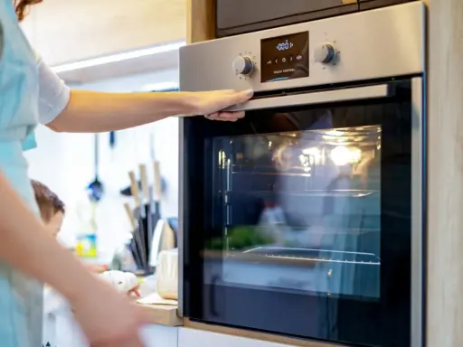 Une main ajuste la porte d'un four encastrable. La lumière intérieure est allumée, prêt pour la cuisson.