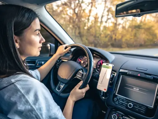 Kobieta prowadzi auto, a telefon z nawigacją zamontowany jest na desce rozdzielczej. Idealne miejsce, gdzie zamontować uchwyt na telefon w samochodzie.