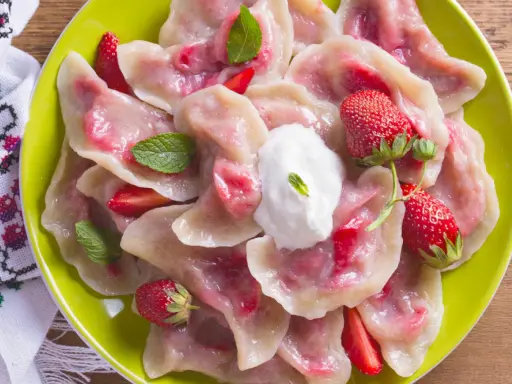 Pyszne pierogi z truskawkami, udekorowane miętą i śmietaną, na zielonym talerzu.