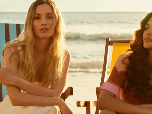 Zwei Frauen entspannen sich am Strand. Die eine mit blonden Haaren, die andere mit braunen Locken. Perfekt für die Haarpflege im Sommer.