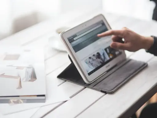 Dłoń wskazuje na ekran tabletu, który wyświetla stronę internetową. Obok leży otwarta książka z grafikami. W tle widać filiżankę. To idealne miejsce do pracy nad projektem, gdzie każdy element, nawet **padding CSS**, ma znaczenie.