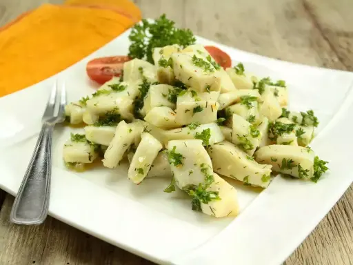 Délicieuse seiche en persillade, servie sur une assiette blanche avec une touche de tomate et de persil frais. Un plat savoureux et léger.