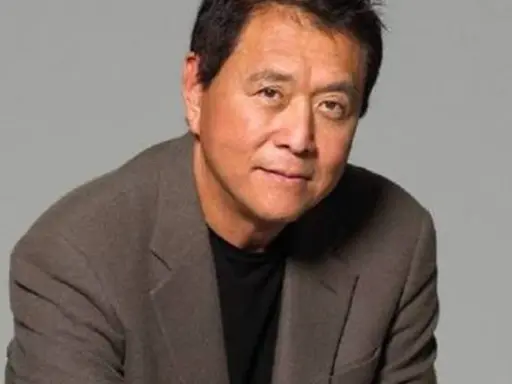 Robert Kiyosaki, autor "Bogatych ojców", w brązowej marynarce i czarnej koszulce, patrzy w obiektyw.