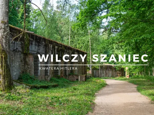 Wilczy Szaniec, dawna kwatera Hitlera, otoczona bujną zielenią. Kamienne mury i leśna ścieżka tworzą atmosferę minionych czasów.